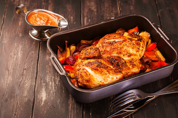 Grilled chicken with baked vegetables and spicy sauce on black wooden background. Selective focus
