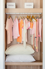 colorful kid's clothes hanging on bar in wooden wardrobe