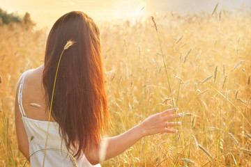 Woman in a wheat field on the background of the setting sun