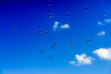 A bunch of soap bubbles flying up into the dark blue sky