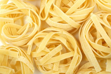 Full background of dry uncooked tagliatelle nest pasta noodles