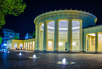 People are sitting in front of illuminated elisenbrunnen in german Aachen.