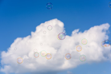 A bunch of colorful soap bubbles flying up into the dark blue sky