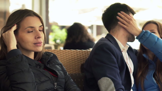 Young, jealous woman sitting next to happy, in love couple in cafe 
