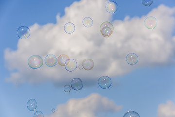 A bunch of colorful soap bubbles flying up into the blue, cloudy sky