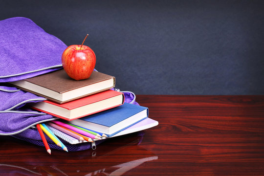 Books, apple, backpack and pencils on wood desk table and black