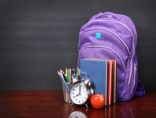 Books, apple, backpack, alarm clock and pencils on wood desk tab