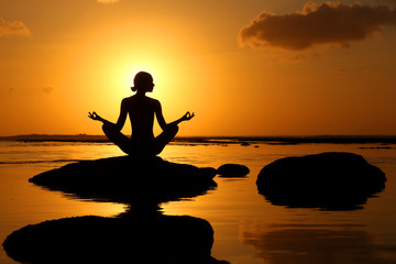 Fototapeta na wymiar Silhouette of woman practicing yoga during sunset at the seaside