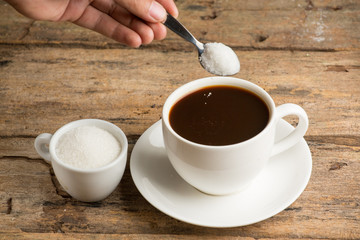 Coffee cup detail and teaspoon. Pouring sugar on coffee cup.