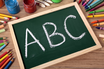 ABC written on a small blackboard on a child student desk with crayons and pencils alphabet...