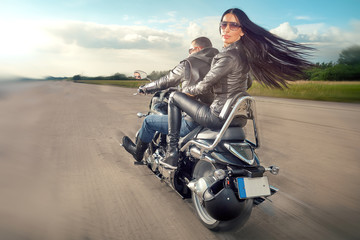Biker Man and woman wearing black leather jackets and stylish sunglasses riding on motorcycle