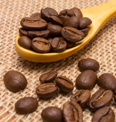 Heap of coffee beans with wooden spoon on jute canvas
