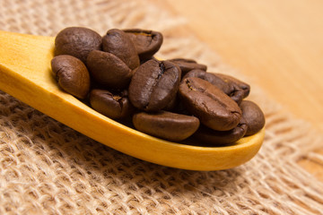 Heap of coffee beans with wooden spoon on jute canvas