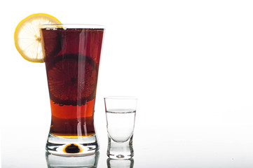 Glass of cola with sliced lemon and shot of vodka