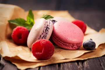 Pink and violet macaroons with fresh berries and mint on dark rustic wooden background. Selective focus