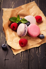 Pink and violet macaroons with fresh berries and mint on dark rustic wooden background. Selective focus