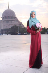 Fototapeta na wymiar high fashion muslim women holding a flower with mosque background at sunset