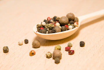 Spoon filled with a mixture of grains of pepper are on a wooden