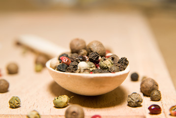 Spoon filled with a mixture of grains of pepper are on a wooden
