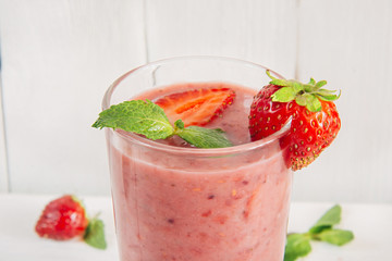 A glass of strawberry smoothie on white wooden table