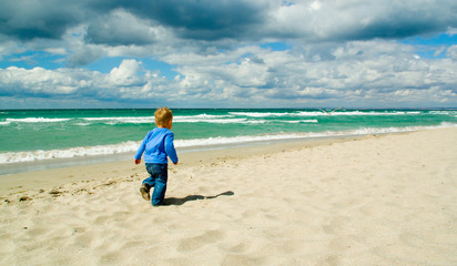 Little boy running along a beach  on a cloudy sky background back view