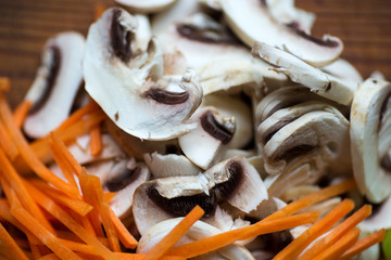 Sliced champignon mushrooms and carrote on a wooden deck