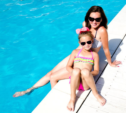 Woman and little girl sitting near swimming pool