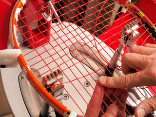 Racquet stringer weaving cross strings of polyester monofilament string in a Tennis racquet on a...