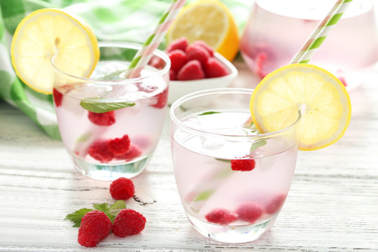 Raspberries and juice in glass on white wooden background