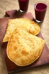Traditional Bolivian Pastel, a deep-fried pastry filled with cheese, a popular street snack, served with api, photographed with natural light (Selective Focus, Focus on the lower half of the pastel)