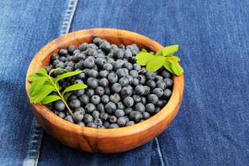 Fototapeta na wymiar Wild blueberries with fresh green leaves in handmade wooden bowl