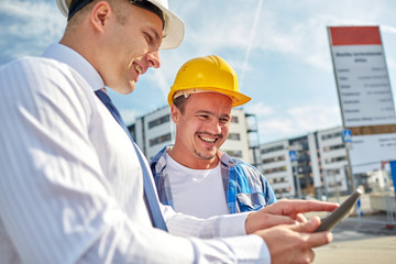 happy builders in hardhats with tablet pc outdoors