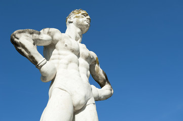 Fototapeta na wymiar Ancient marble statue of muscular athlete boxer with sculpted body against bright blue sky