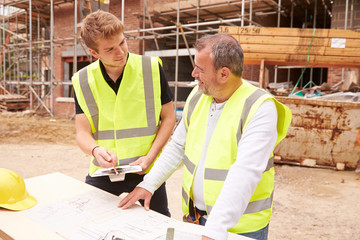 Builder On Building Site Discussing Work With Apprentice