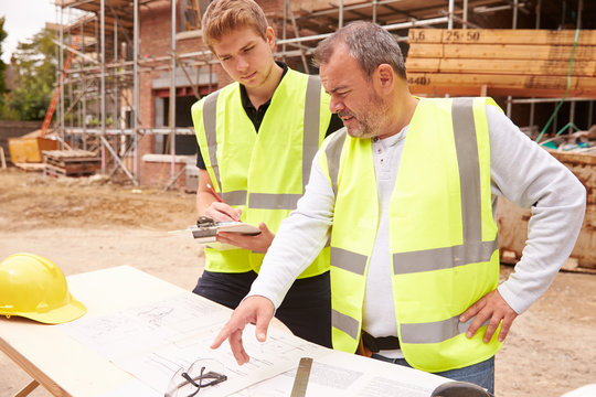 Builder On Building Site Discussing Work With Apprentice