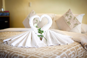 View of two white towels swans on bed sheet in hotel