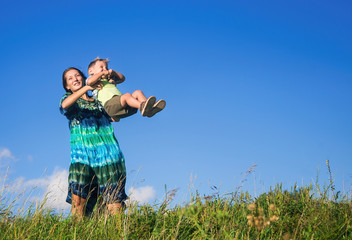 Happy mother with son fun on walk in high grass against blue sky