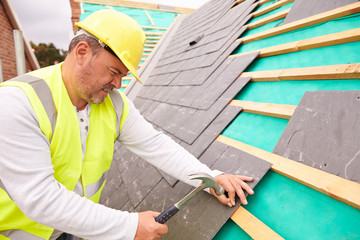 Construction Worker On Building Site Laying Slate Tiles