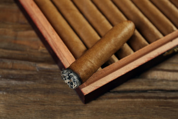 Cigars and burning one in box on wooden table, closeup