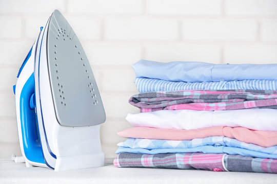 Electronic ironing and pile of clothes on board on brick wall background