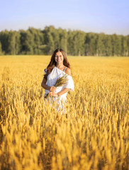 Smiling beautiful girl in wheat field with ears in his hands