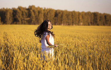 Smiling beautiful girl spinning in a field of wheat with ears