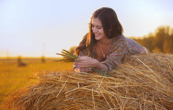 Smiling beautiful girl in the hay watching the wheat grass at sunset