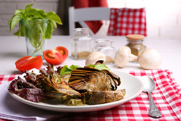 Roasted artichokes on plate, on kitchen table background