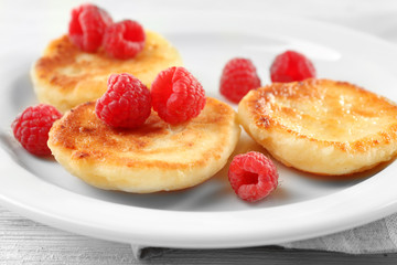 Fritters of cottage cheese with raspberries in plate on table, closeup