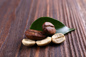 Green and brown coffee beans with leaf on wooden background