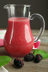 Glass jug of blackberry smoothie on wooden table, closeup