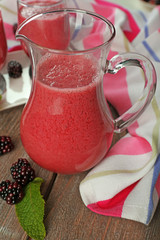 Glass jug of blackberry smoothie on wooden table, closeup