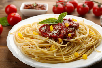 Spaghetti with tomato sauce, paprika and cheese on white plate, on color wooden background
