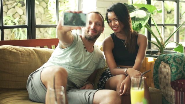 Happy couple taking selfie photo with cellphone sitting in cafe 
